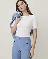 A woman in a white ribbed top and blue pants poses with a blue jacket draped over her shoulder against a plain background. carousel Product Image 1