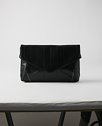 A black, textured envelope clutch rests on a white surface against a plain white background. carousel Product Image 1