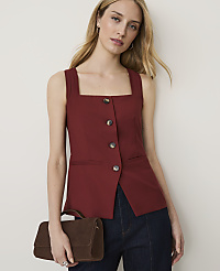 A woman in a maroon square-neck top and dark jeans holds a brown handbag against a plain wall. carousel Product Image 1