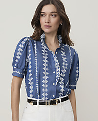 A woman in a blue, embroidered blouse and white pants stands against a plain background. carousel Product Image 1