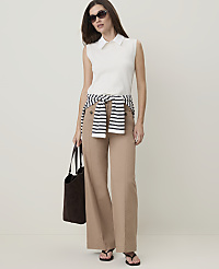 A woman in a white sleeveless polo shirt, tan wide-leg pants, and a striped sweater tied around her waist stands against a plain, light-colored background, holding a dark tote bag. carousel Product Image 1
