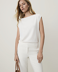 A woman in a white top and pants stands against a plain white background, holding a brown bag. carousel Product Image 1