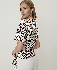A woman in a patterned top and white pants stands against a plain white background. carousel Product Image 2