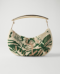 A cream-colored, crescent-shaped handbag with a green botanical pattern and a gold handle rests against a plain white background. carousel Product Image 1
