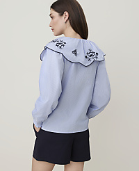A woman in a blue and white striped blouse with a large ruffled collar stands against a plain white background. carousel Product Image 2