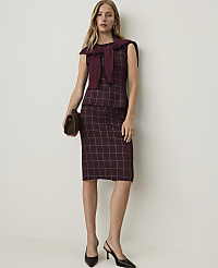 A woman in a burgundy plaid dress and sweater draped over her shoulders stands against a plain white background, holding a brown clutch. carousel Product Image 1