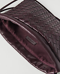 A woven burgundy leather clutch with a satin lining and a brand tag is shown against a white background. carousel Product Image 2