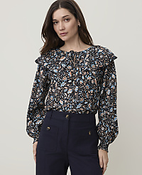 A woman in a floral blouse and dark pants stands against a plain white background. carousel Product Image 1