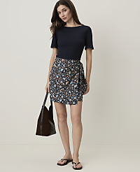 A woman in a navy top and floral wrap skirt stands with a brown tote bag, against a plain, light-colored background. carousel Product Image 1