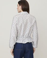 A woman wearing a white patterned blouse and blue jeans stands against a plain, light-colored background. carousel Product Image 2