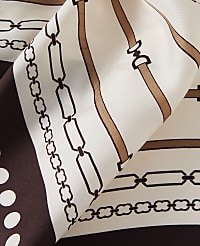 A cream-colored silk scarf with a brown chain and buckle pattern is folded in the foreground, with a plain cream background. carousel Product Image 2