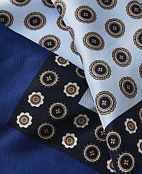 A close-up of a silk scarf with a geometric pattern of circular motifs in shades of blue and brown is laid out against a solid blue background. carousel Product Image 2