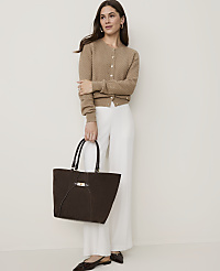 A woman in a brown cardigan and white pants holds a dark brown tote bag in front of a plain, light-colored background. carousel Product Image 4