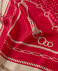 A vibrant red silk scarf with a white equestrian-themed pattern is draped in the foreground, while a blurred, neutral background provides a soft contrast. carousel Product Image 3