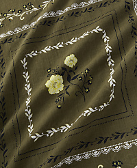 A close-up view of a khaki-colored bandana features a central diamond pattern with yellow flowers and white leafy borders, set against a textured fabric background. carousel Product Image 3