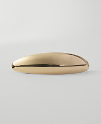 A polished, elongated gold object rests on a plain, light gray surface against a soft, white background. carousel Product Image 1