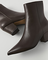 A pair of pointed-toe brown leather ankle boots with block heels rests on a light gray surface. carousel Product Image 2