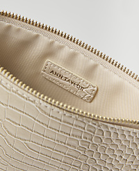 A close-up of a cream-colored, croc-embossed clutch bag with a gold zipper is shown against a plain white background. carousel Product Image 2