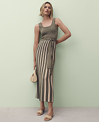 A woman in a ribbed knit dress with a belted waist and sandals stands against a pale green background, holding a small straw bag. carousel Product Image 4