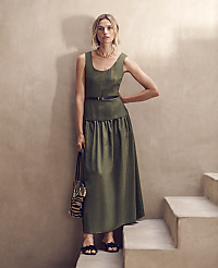 A woman in a green dress stands on a staircase against a textured wall. carousel Product Image 3
