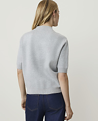 A woman in a grey short-sleeved sweater and dark jeans stands against a plain, light-colored background. carousel Product Image 2
