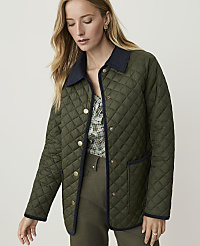 A woman in a quilted green jacket stands against a plain, light-colored background. carousel Product Image 1