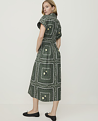 A woman in a green, patterned midi dress and black flats stands against a plain, light-colored background. carousel Product Image 2
