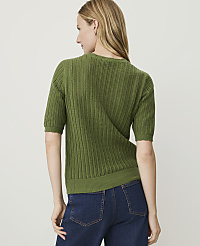 A woman in a green short-sleeved sweater and blue jeans stands against a plain white background. carousel Product Image 2