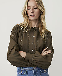 A blonde woman in a green blouse and blue jeans stands with her arms crossed against a plain white background. carousel Product Image 1