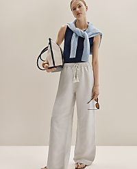 A woman in wide-leg linen pants and a striped tank top stands against a plain, light-colored background, holding a tote bag and sunglasses. carousel Product Image 4