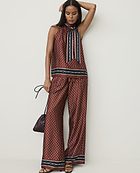 A woman in a patterned rust-colored halter top and wide-leg pants stands against a plain white background, holding a small dark purse. carousel Product Image 4