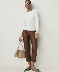 A woman in a white sweater and brown leather pants stands against a plain white background, holding a beige handbag and wearing checkered flats. carousel Product Image 1