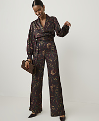 A smiling woman in a patterned wrap top and wide-leg pants holds a clutch against a plain white background. carousel Product Image 1