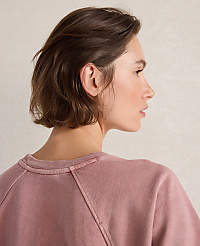 A woman with short brown hair in a pink sweatshirt is shown against a plain, light-colored background. carousel Product Image 2