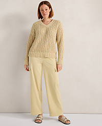 A woman in a beige v-neck sweater and light yellow cargo pants stands against a textured, light-colored wall. carousel Product Image 1