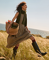 A woman in a dress and boots walks through tall grass carrying a basket, with the ocean and sky in the background. carousel Product Image 7