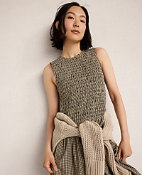 A woman in a textured sleeveless dress and a beige sweater tied around her waist stands against a plain, light-colored wall. carousel Product Image 3
