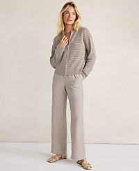 A woman in a textured gray zip-up sweater and wide-leg beige pants stands against a neutral, textured background. carousel Product Image 4