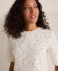A woman with curly dark hair wears a white eyelet top against a plain, light background. carousel Product Image 2