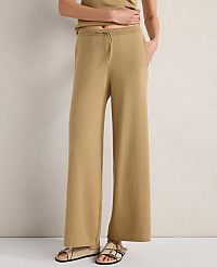 A person stands in tan wide-leg pants and sandals against a neutral, textured wall. carousel Product Image 1