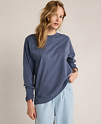 A woman in a blue sweatshirt and light blue pants stands against a plain, light gray background. carousel Product Image 1