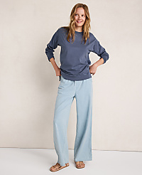 A smiling woman in a blue sweatshirt and light blue wide-leg pants stands against a textured, light-colored wall. carousel Product Image 4