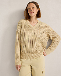 A woman in a beige v-neck sweater and light-colored pants stands against a textured gray wall. carousel Product Image 1