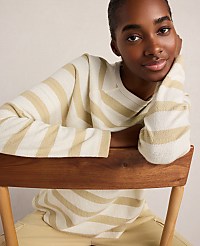 A young woman in a striped sweater leans on a wooden chair against a plain background. carousel Product Image 3