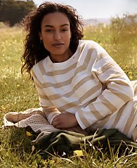 A woman with curly dark hair lies on a blanket in a grassy field with yellow wildflowers, while a blurred landscape stretches out behind her. carousel Product Image 6