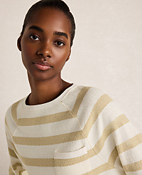 A woman with dark skin and short hair wears a cream and tan striped sweater with a pocket in the foreground, against a softly lit, neutral background. carousel Product Image 2