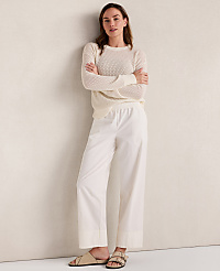 A woman in a cream sweater and white pants stands with her arms crossed against a textured cream wall. carousel Product Image 3