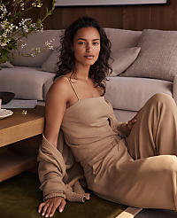 A woman in a beige outfit sits on a green rug in the foreground, with a light-colored sofa and a wooden wall in the background. carousel Product Image 6