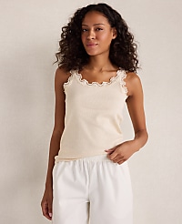 A woman in a cream-colored lace-trimmed tank top and white pajama bottoms stands against a plain, light-colored background. carousel Product Image 1