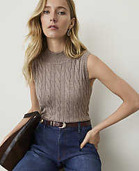 A woman in a cable-knit mock neck top and dark jeans poses against a plain, light background. carousel Product Image 1